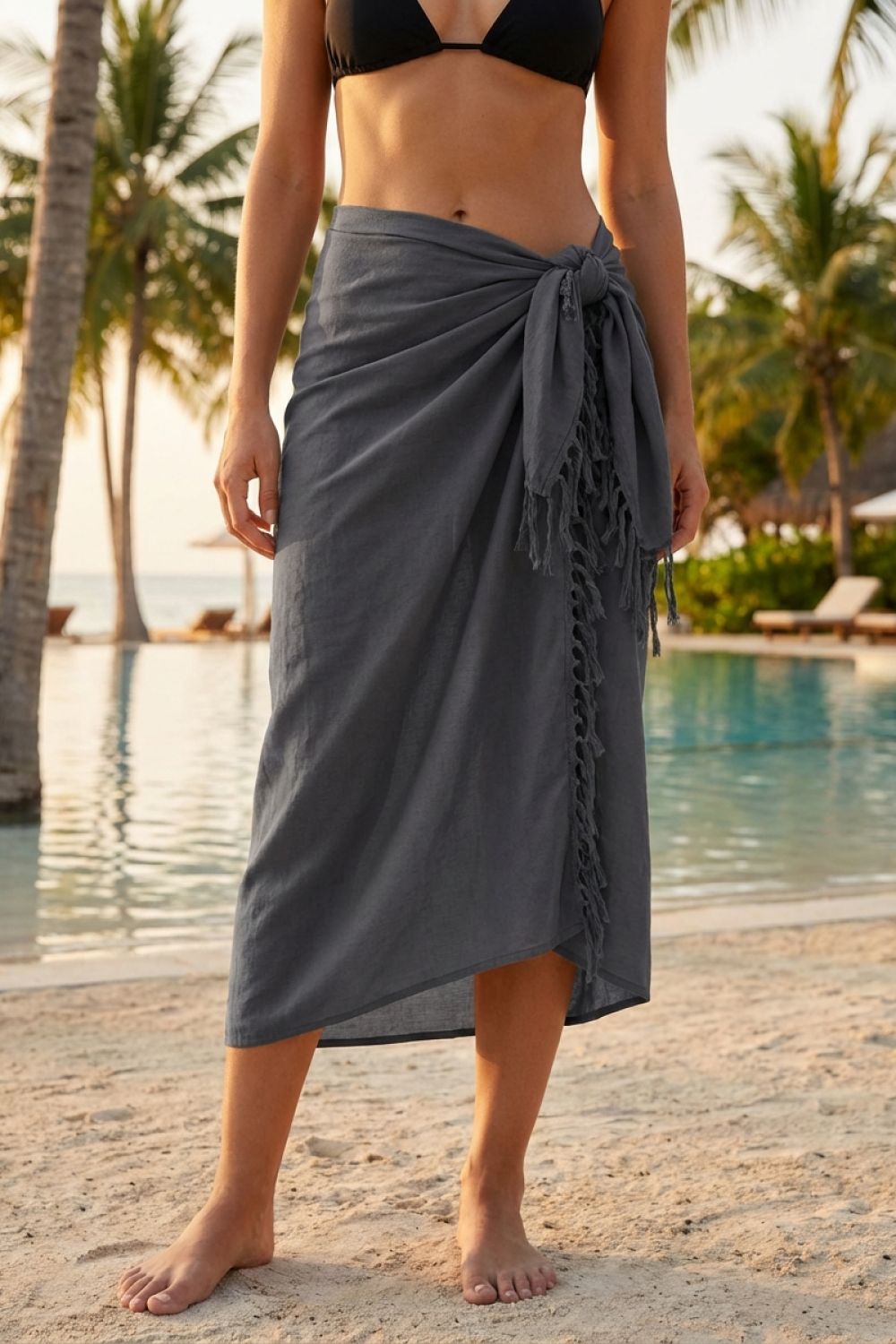 Person wearing a gray sarong by a pool with palm trees in the background