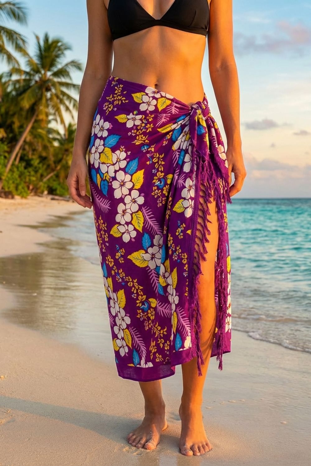 Person wearing a purple floral sarong on a beach with palm trees and ocean in the background