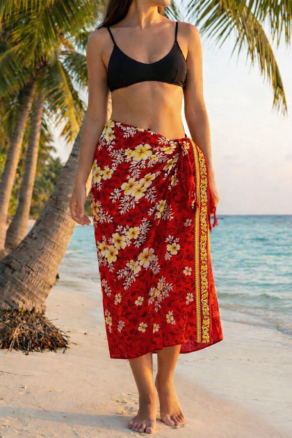 Woman in a red floral sarong standing on a beach with palm trees and ocean in the background