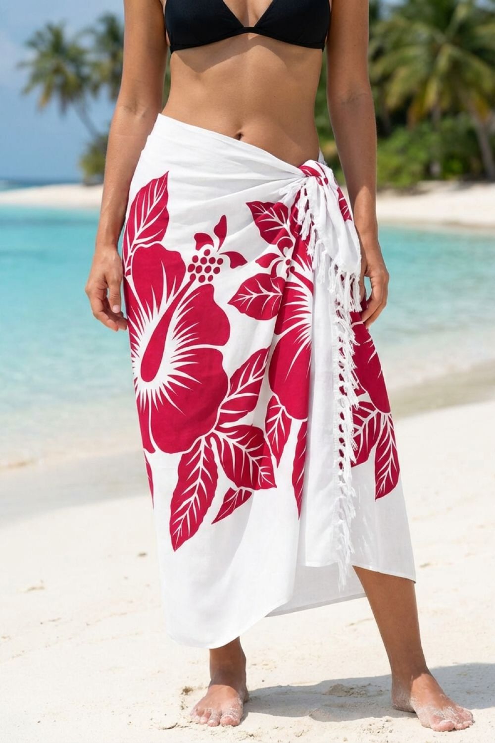 Person wearing a white sarong with pink floral patterns on a beach.